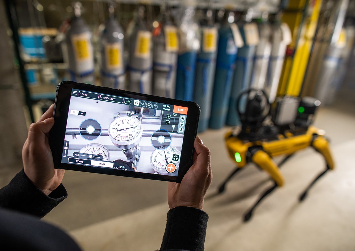 An operator using a tablet to remotely control Spot to monitor gas pressure gauges in an industrial setting.