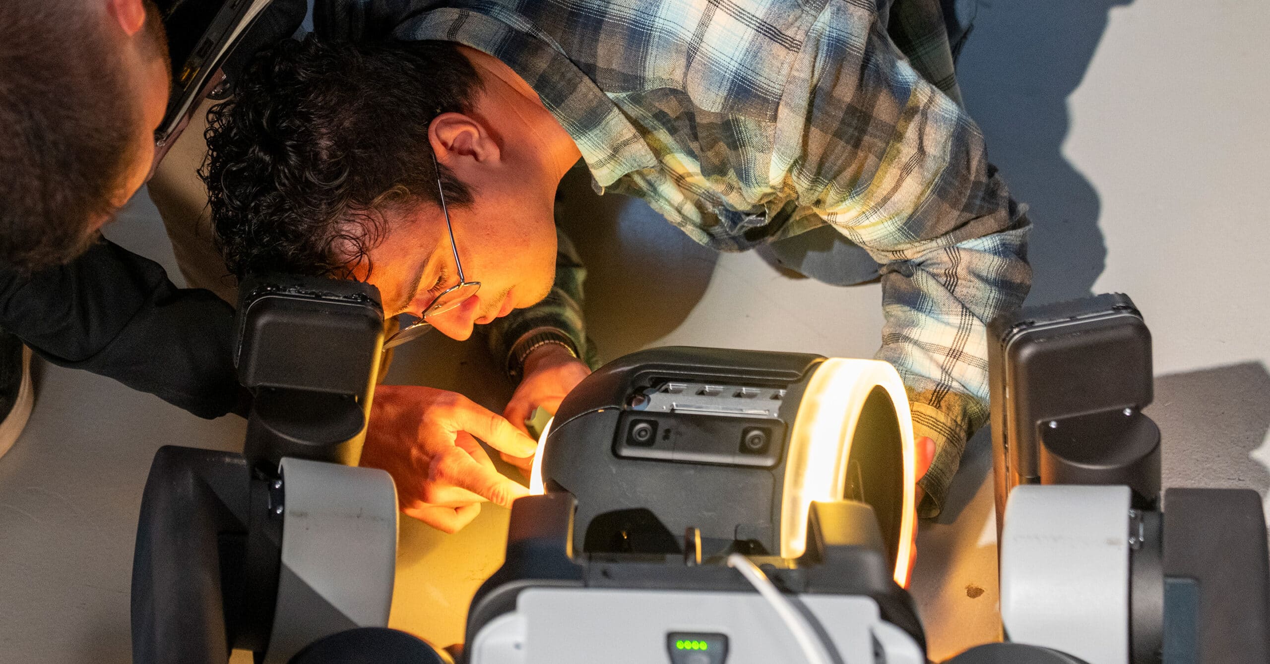 Two engineers work on the Atlas robot, lit by the glow from it's lights