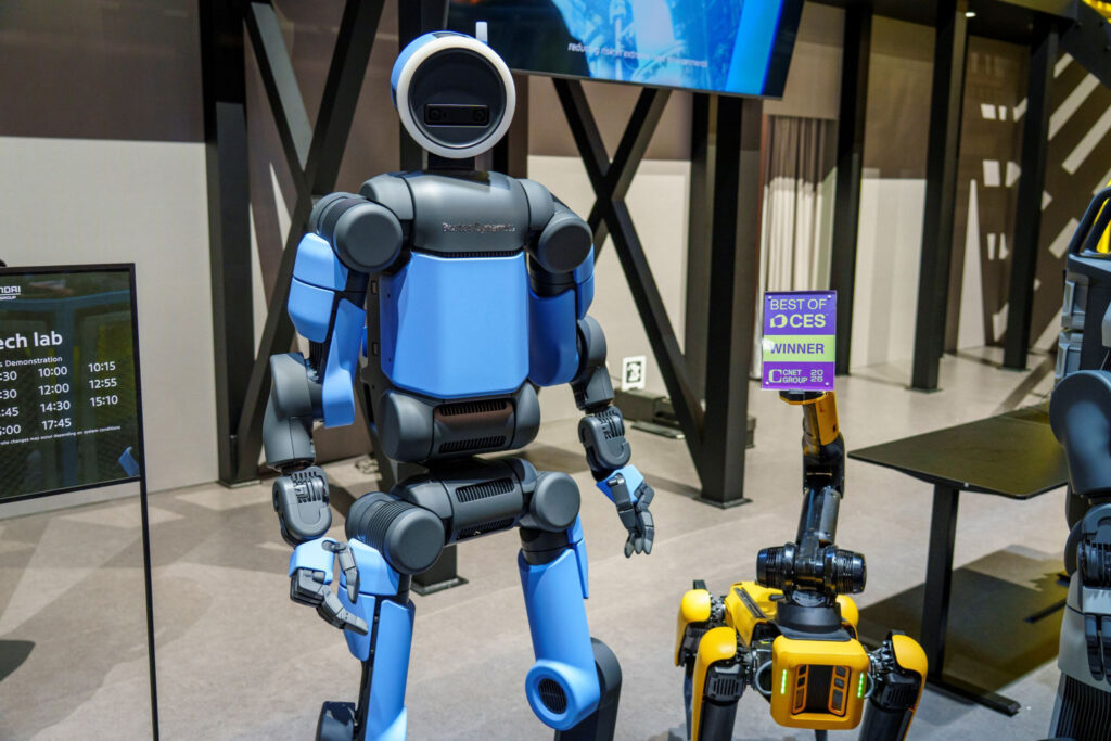 The Atlas robot stands next to a Spot robot holding a Best of CES placard