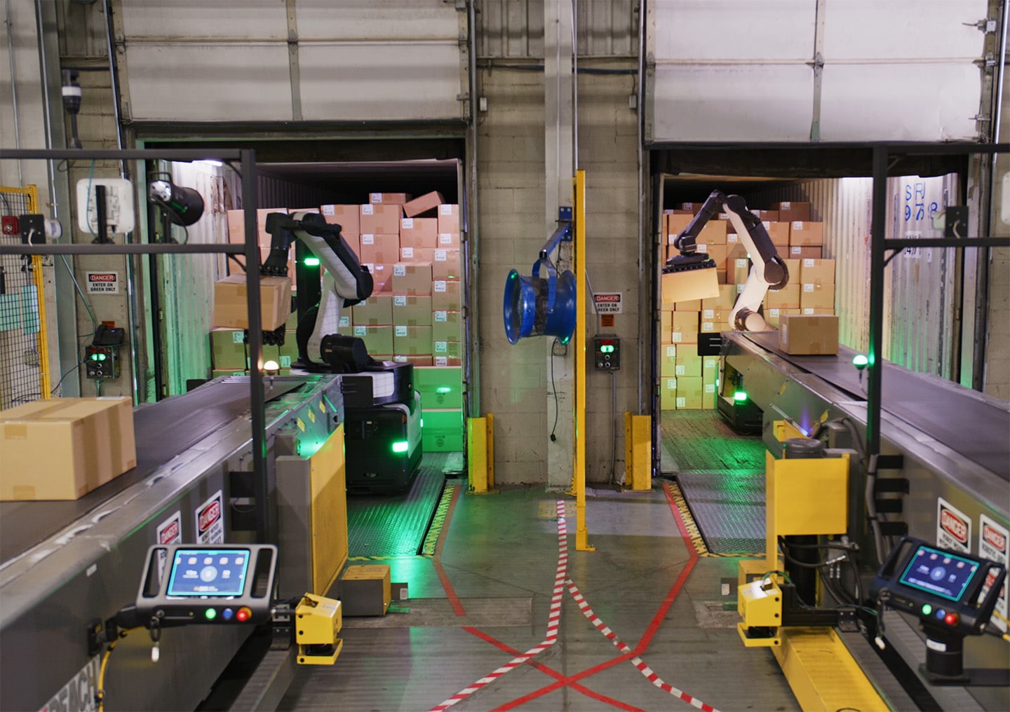 Two robots unload boxes to conveyor belts in a warehouse.