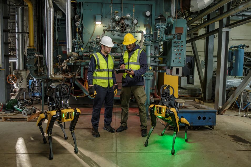 Two reliability engineers standing beside two Spot robots in an industrial facility